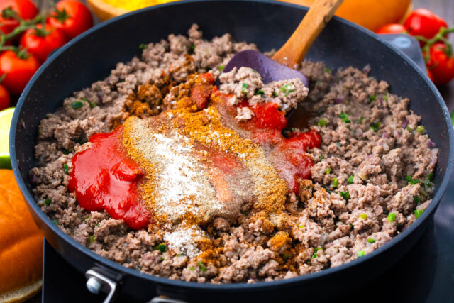 Adding spices and tomato sauce to ground beef.
