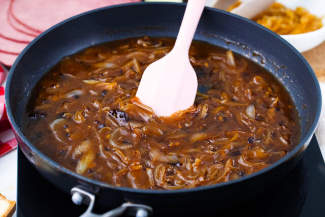 Rich caramelized onion au jus sauce thickening in a skillet, ready for dipping.