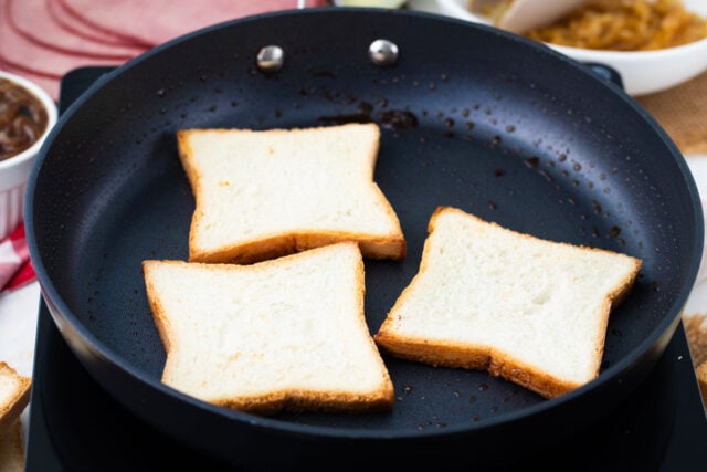 Buttered white bread slices browning in a cast iron skillet for grilled cheese.