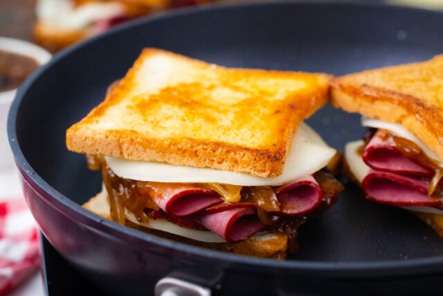 French dip grilled cheese sandwich cooking in a skillet, pressed with a spatula until golden brown.