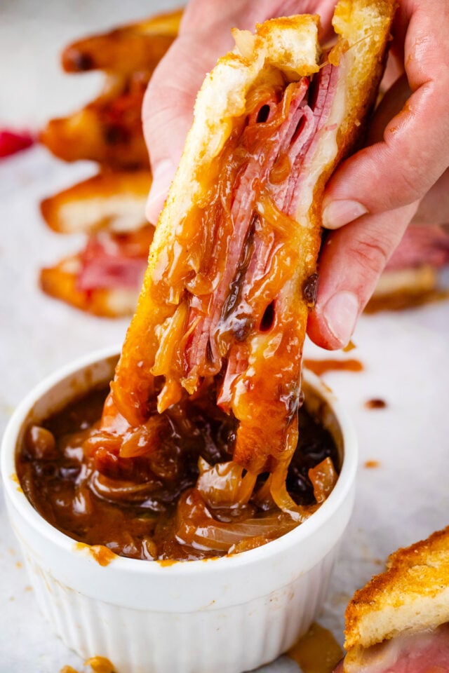 Dipping a French dip grilled cheese sandwich into a bowl of warm au jus sauce.