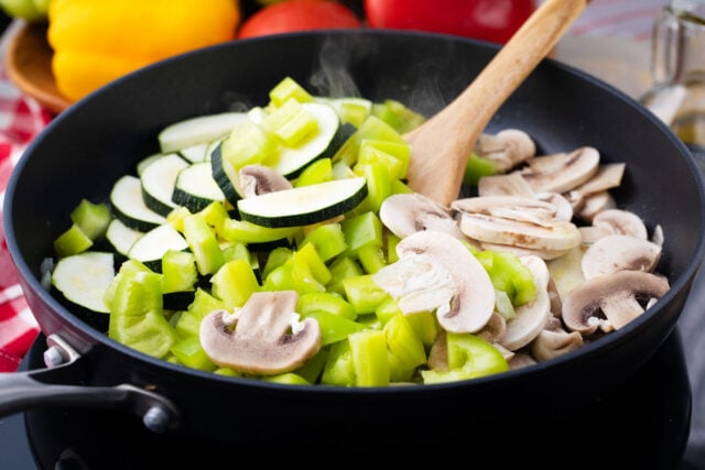 Cooking zucchini, bell peppers, and mushrooms in a skillet.