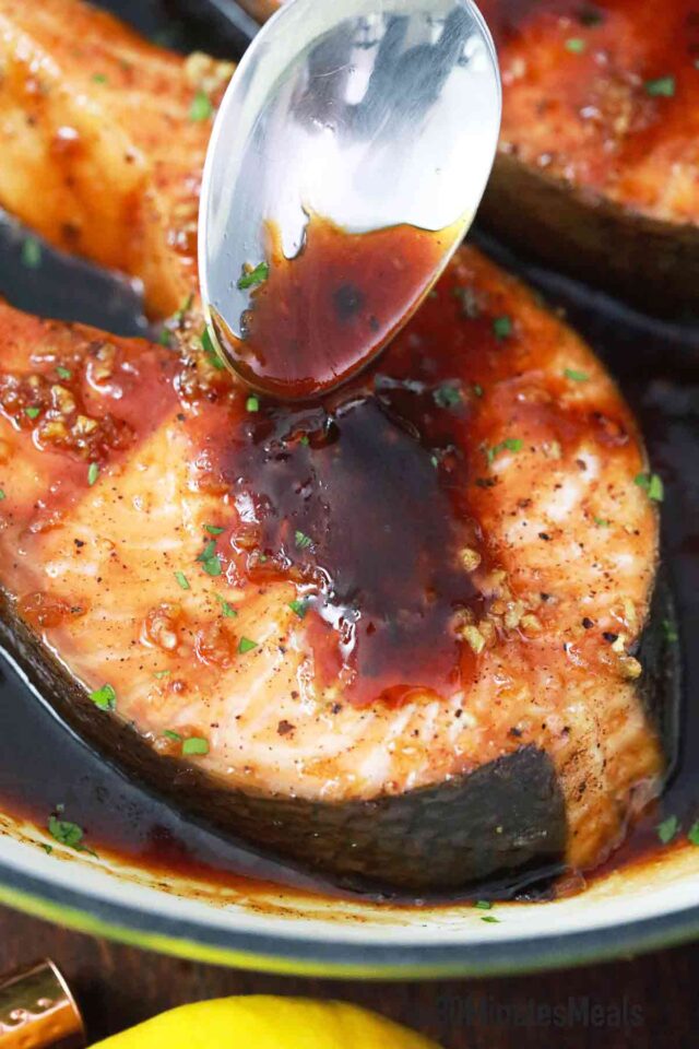 spooning sauce on top of a salmon steak