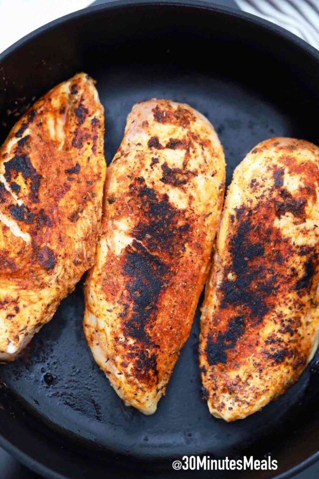 three blackened chicken breasts in a cast iron pan