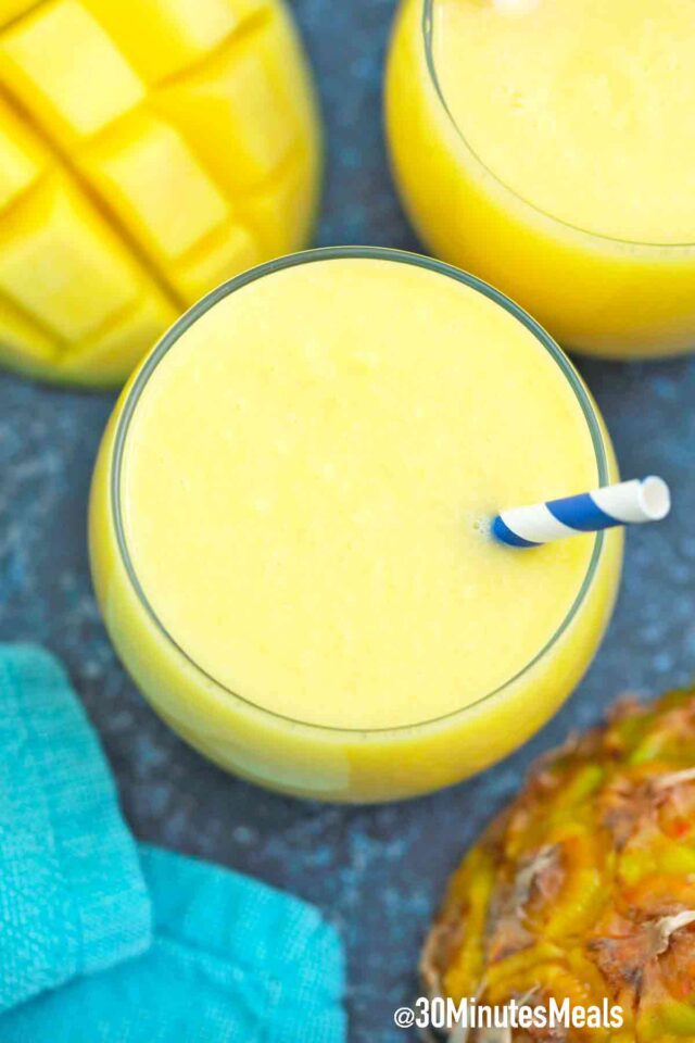 mango pineapple smoothies with fresh mango and pineapple next to it