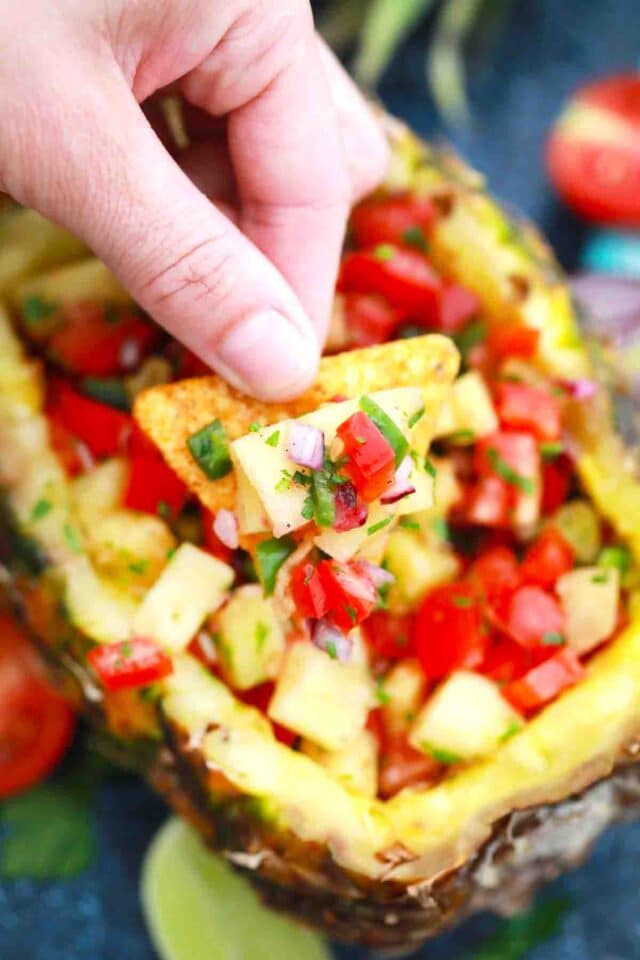 holding a corn chip topped with Pineapple Mango Salsa