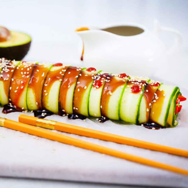 cucumber sushi roll with chopsticks in front of it and avocado in the background