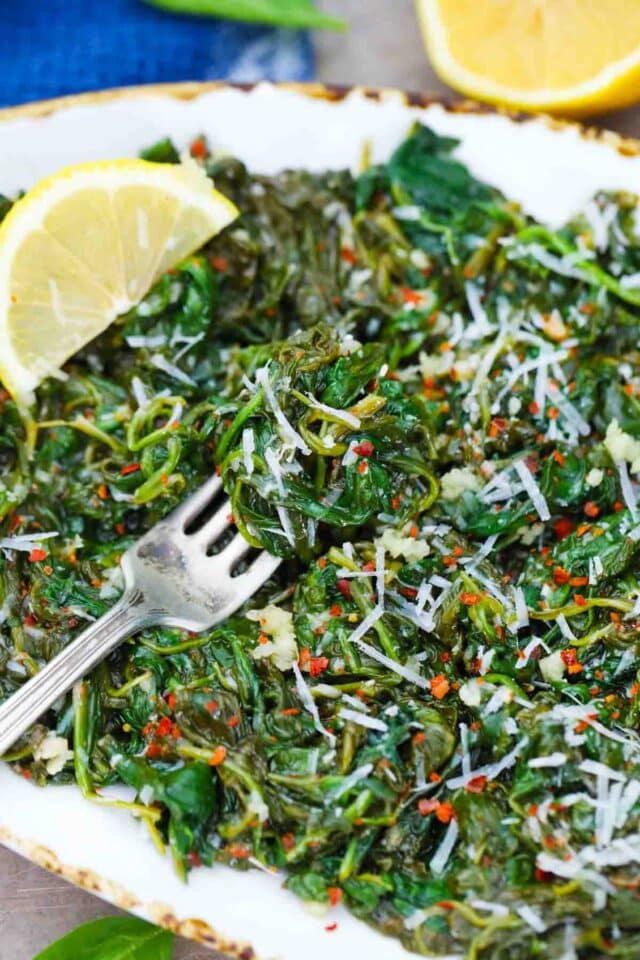 a platter with sauteed spinach topped with grated parmesan and a fork placed on the side