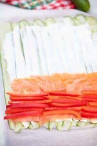 adding bell pepper and smoked salmon to cucumber and cream cheese roll