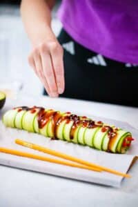 sprinkling sesame seeds on top of a cucumber sushi roll