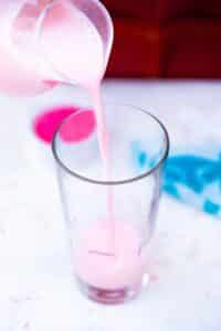 pouring pink milk into a tall glass