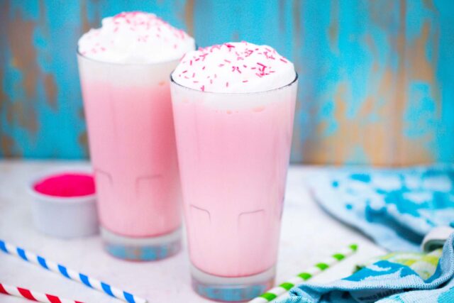 two tall glasses of pink angel milk and pink sprinkles in the background