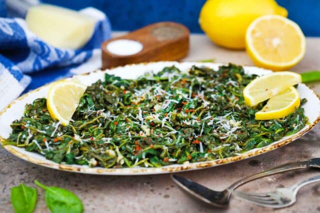 an oval platter with sauteed spinach served with lemon wedges