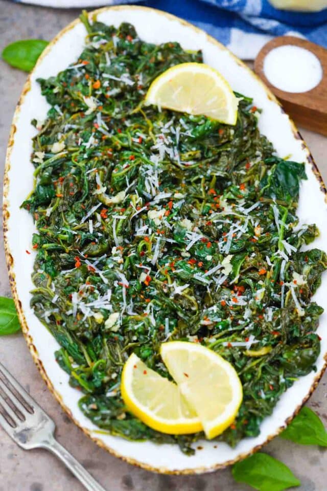 overhead shot of a serving plate with sauteed spinach and lemon wedges