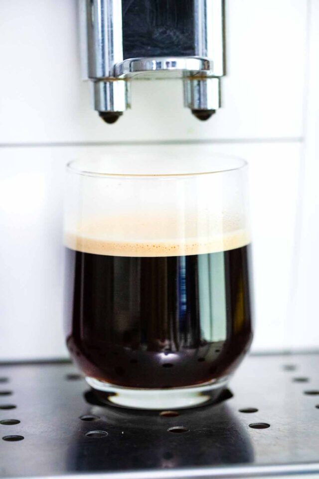 a glass with espresso next to a coffee machine