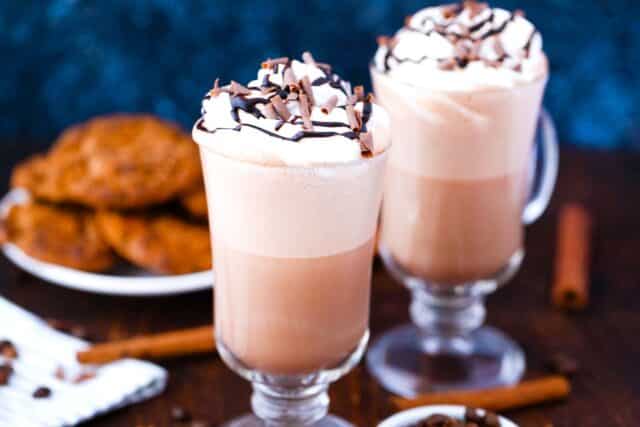 two mocha lattes on a table with cookies in the background