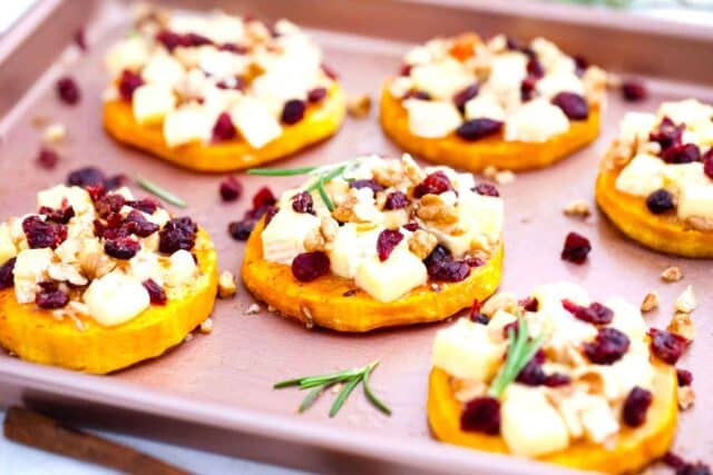 baked butternut squash brie topped with cranberries and rosemary on a baking sheet