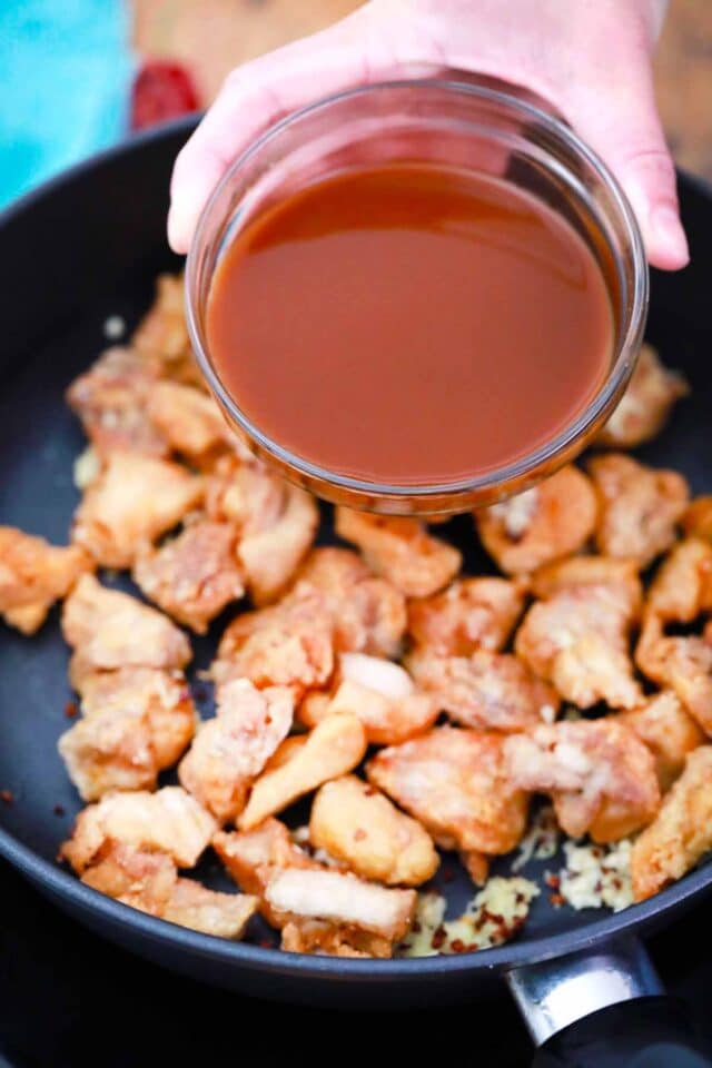 adding spicy sauce to fried chicken in a pan