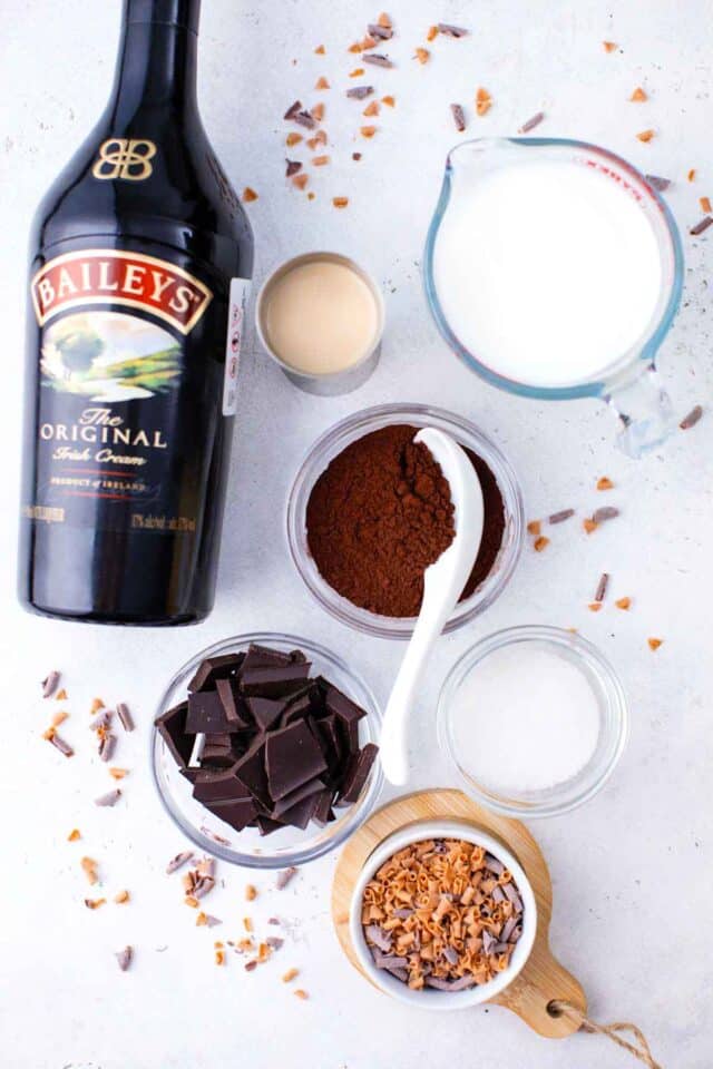 baileys hot chocolate ingredients in bowls on a table next to a bottle of Baileys