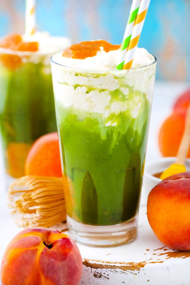 A glass of iced peach matcha freddo with peach puree.