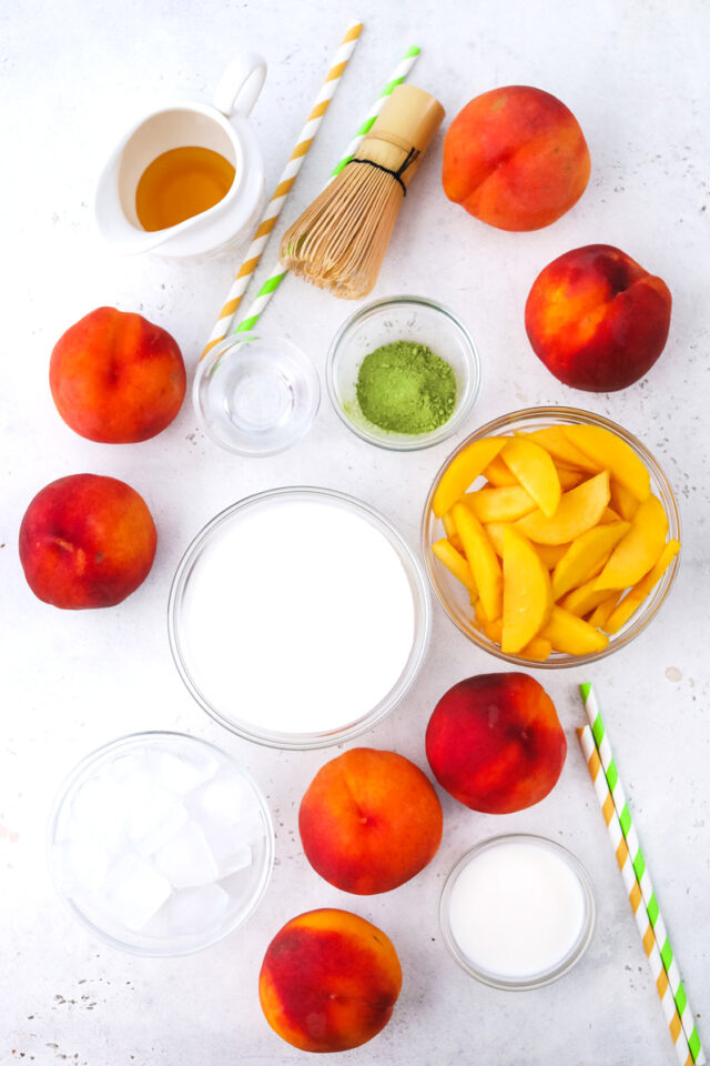 Overhead shot of peach matcha freddo ingredients in bowls on a white surface.